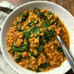 white bowl of soup with fresh spinach and spoon