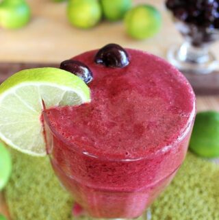 cherry lime slushie in large glass with lime slice