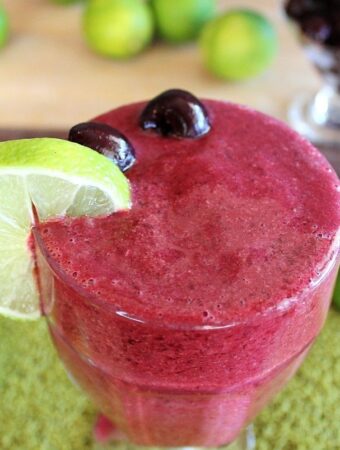 cherry lime slushie in large glass with lime slice