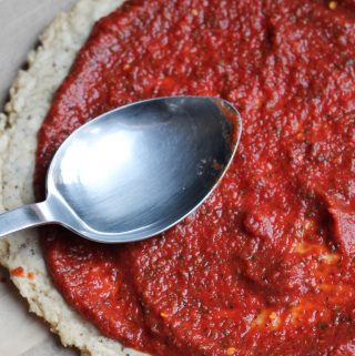 Spoon spreading pizza sauce on pizza crust