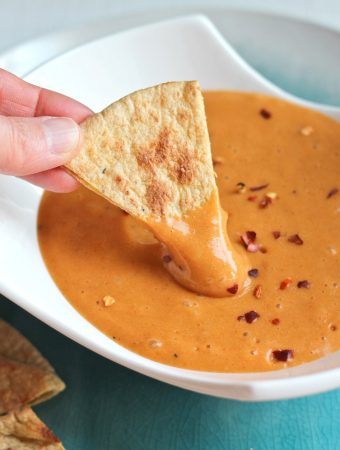 hand dipping chip into cheese sauce in bowl