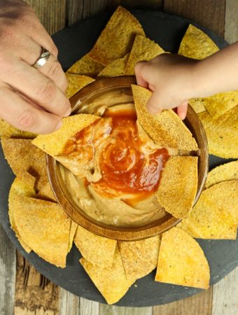 2 hands dipping chips into wood bowl of cheese