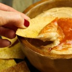 hand dipping chip into bowl of cheese