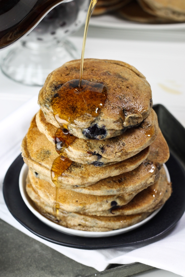 Syrup pouring over fluffy stack of vegan blueberry pancakes