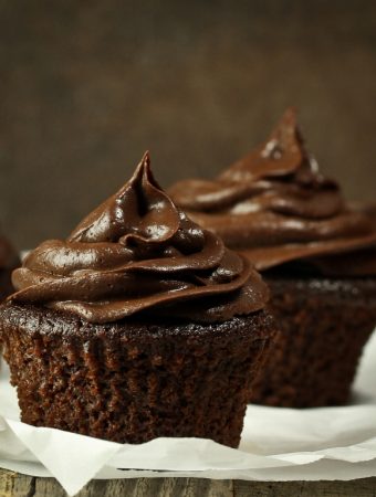 3 chocolate cupcakes with frosting on parchment paper