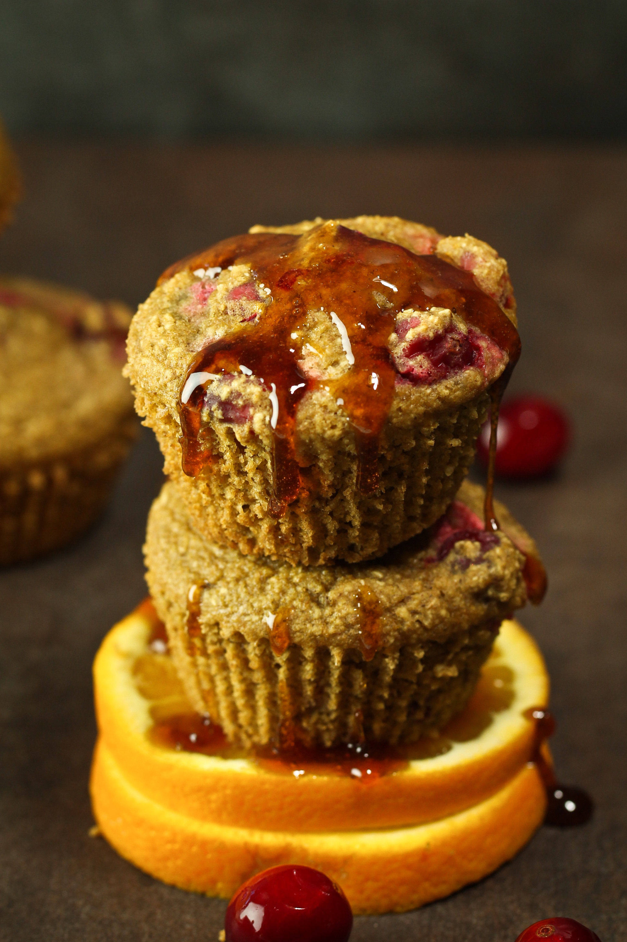 Stack of vegan cranberry orange muffins with orange glaze dripping