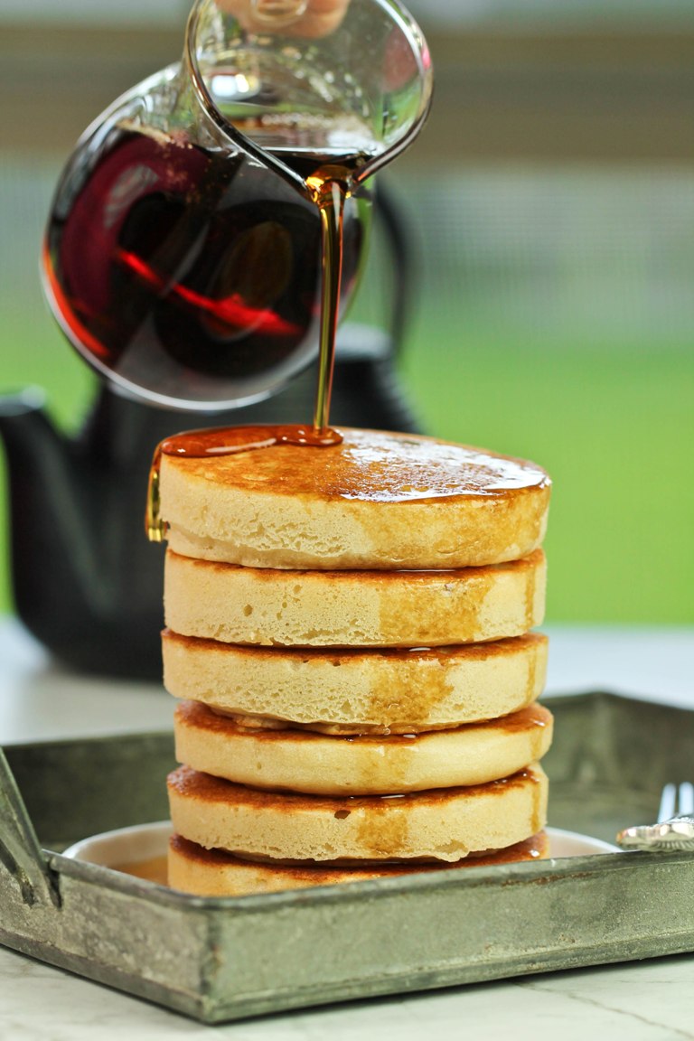 Syrup bottle pouring syrup over a stack of vegan buttermilk pancakes.