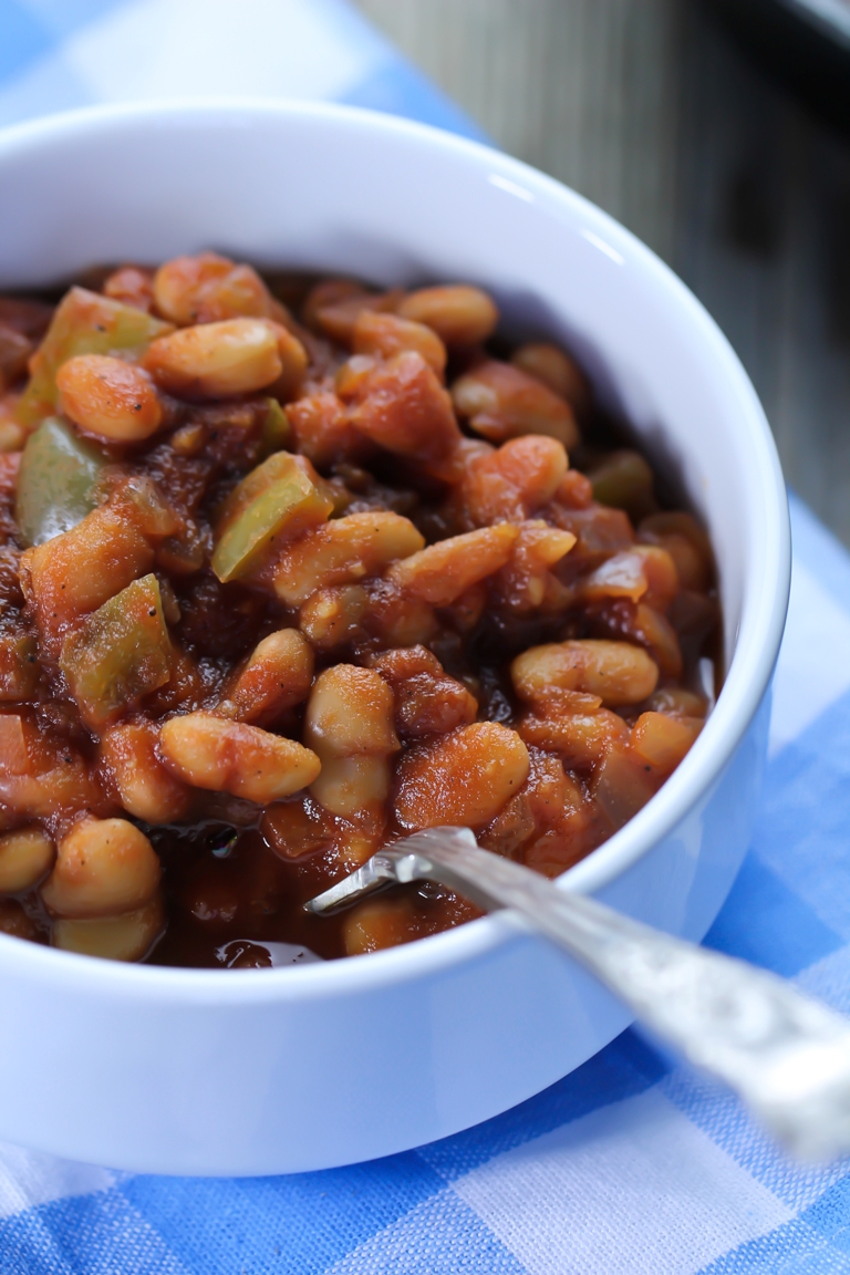 barbecue baked beans in white bowl on blue checkered napkin