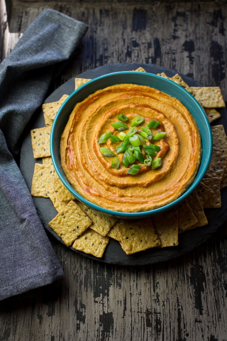 Overhead image of a bowl of spicy vegan buffalo hummus and green onions.