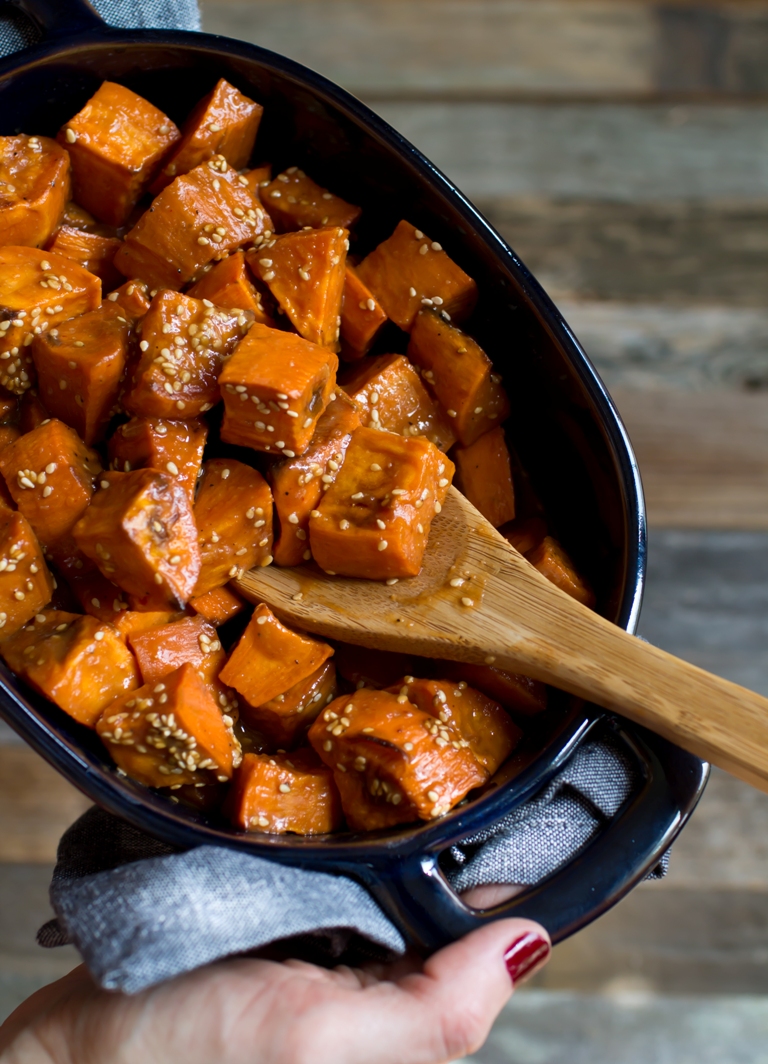 Hands holding dish of miso glazed sweet potatoes and wooden spoon