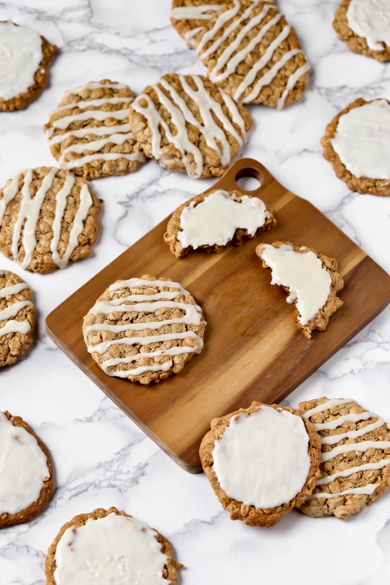 Scattered vegan iced oatmeal cookies on white marble
