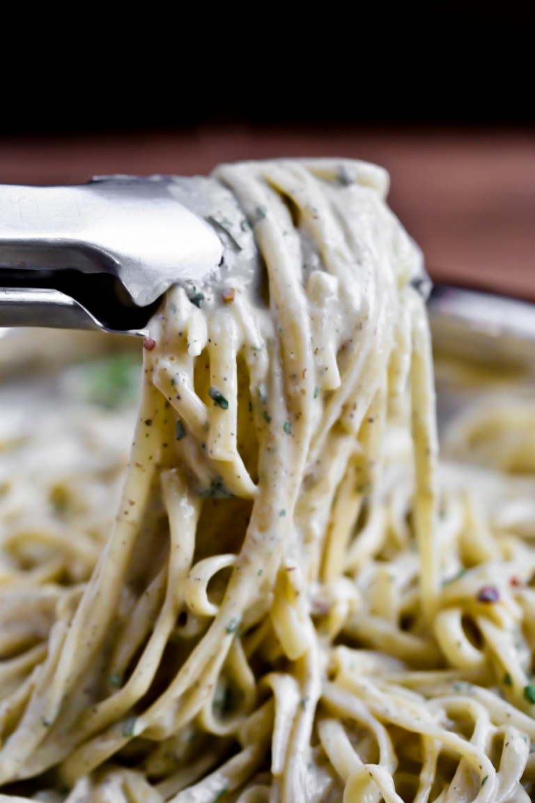 Closeup view of tongs holding vegan alfredo noodles