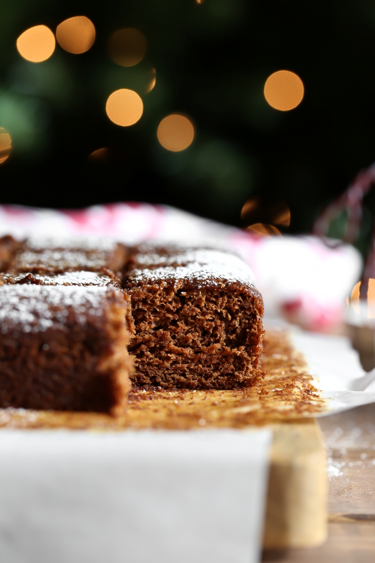 closeup of gingerbread cake slice with powdered sugar on wood platter