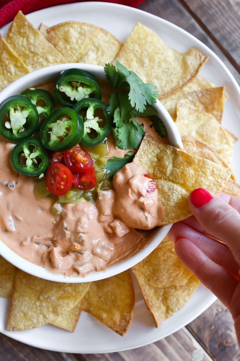 Vegan queso cheese dip in a bowl with hand dipping a chip in the queso.