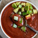spoon in tomato soup with chopped avocado