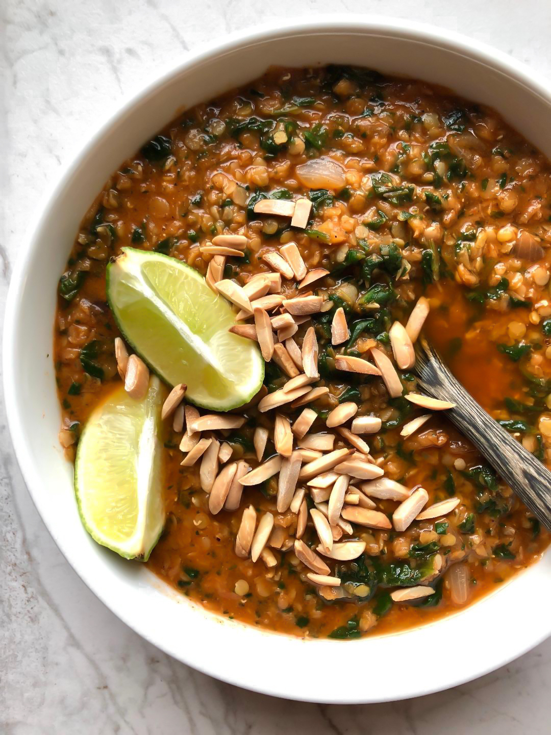 wood spoon spooning vegan red lentil curry with slivered almonds