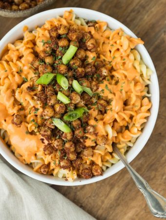 Closeup of plate of vegan pimento cream sauce over fusilli pasta with smoky chicpeas and green onions.