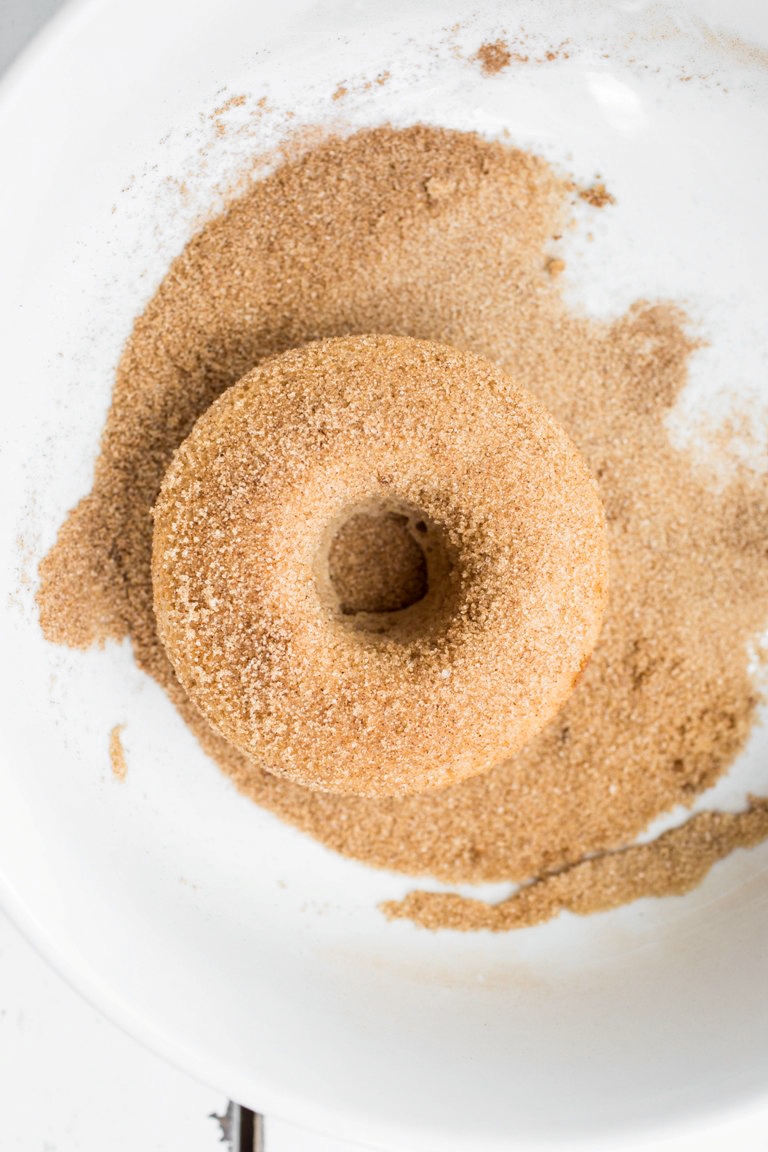 Vegan cinnamon sugar donut in bowl of sugar