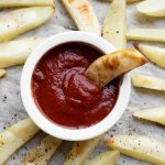 Potato fry sitting in white bowl of ketchup