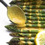 Spoon drizzling lemon ginger sauce on top of baked asparagus