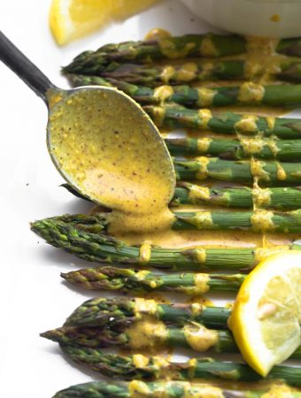 Spoon drizzling lemon ginger sauce on top of baked asparagus