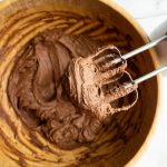 beaters showing chocolate frosting above wooden bowl