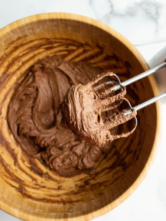 beaters showing chocolate frosting above wooden bowl