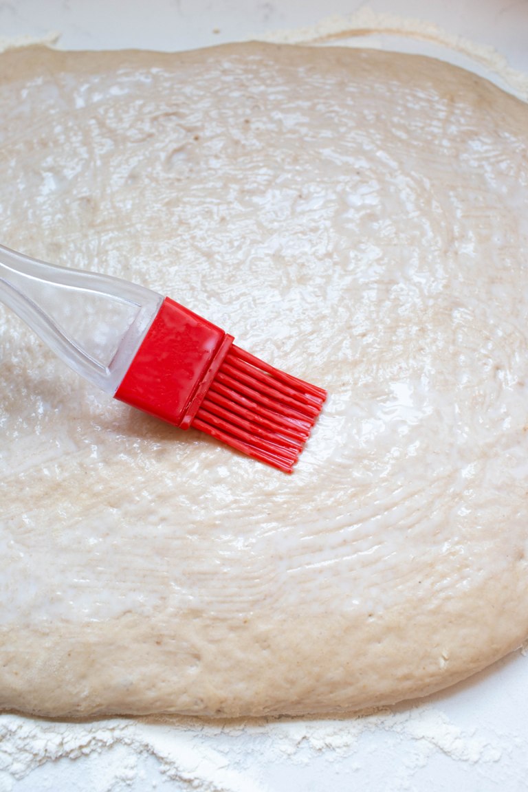 pastry brush spreading coconut milk on top of rolled out dough