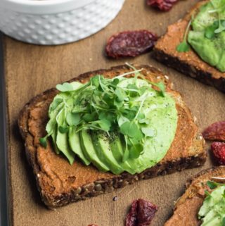 slice of avocado toast on wooden board with microgreens on top