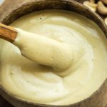 closeup of wooden spoon dipping into caesar dressing in wooden bowl