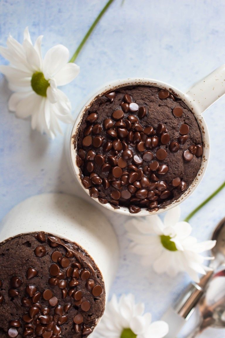 overhead view of 2 cooked chocolate mug cakes with white flowers beside them