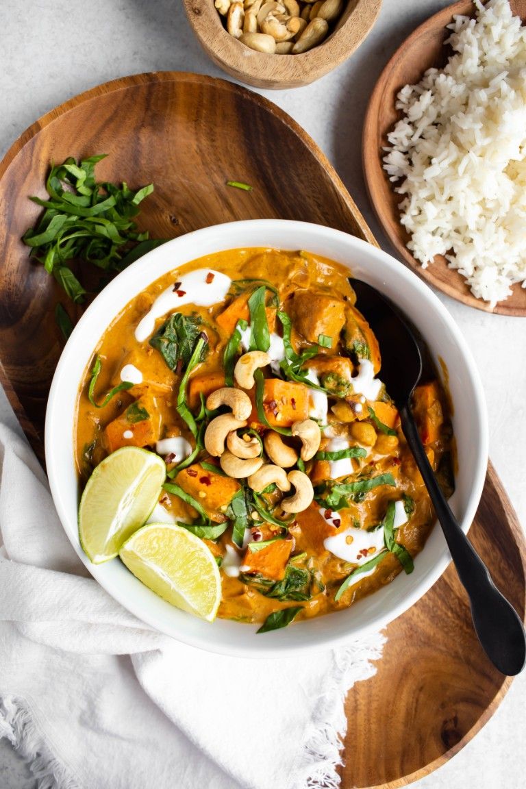 overhead view of white bowl of sweet potato curry with limes and cashews