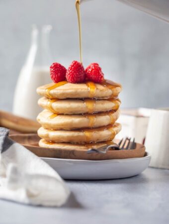stack of vegan pancakes on round wood plate with raspberries on top