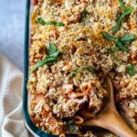 closeup of wooden spoon spooning out some baked ziti from casserole dish