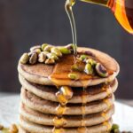 pouring maple syrup over stack of pancakes
