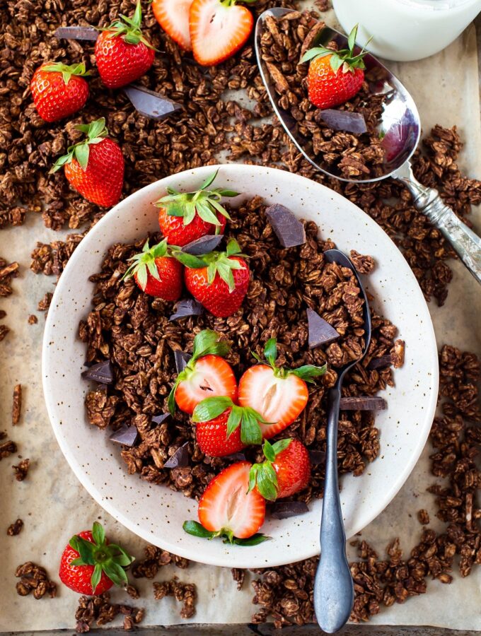 bowl of healthy chocolate granola with spoon and fresh strawberries on tray of granola