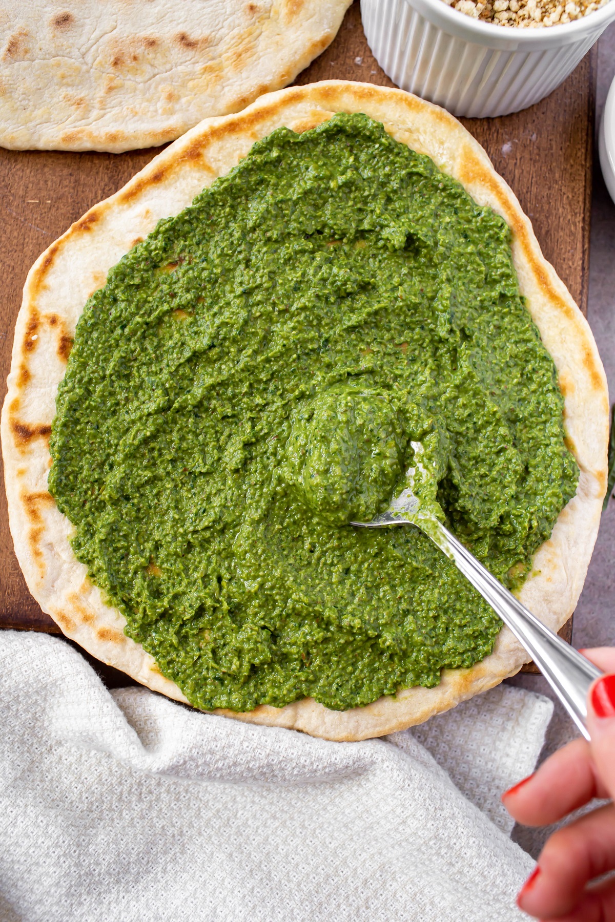 spreading vegan spinach pesto on flatbread with spoon