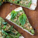 closeup of vegan pesto pizza slices on flatbread on wood platter