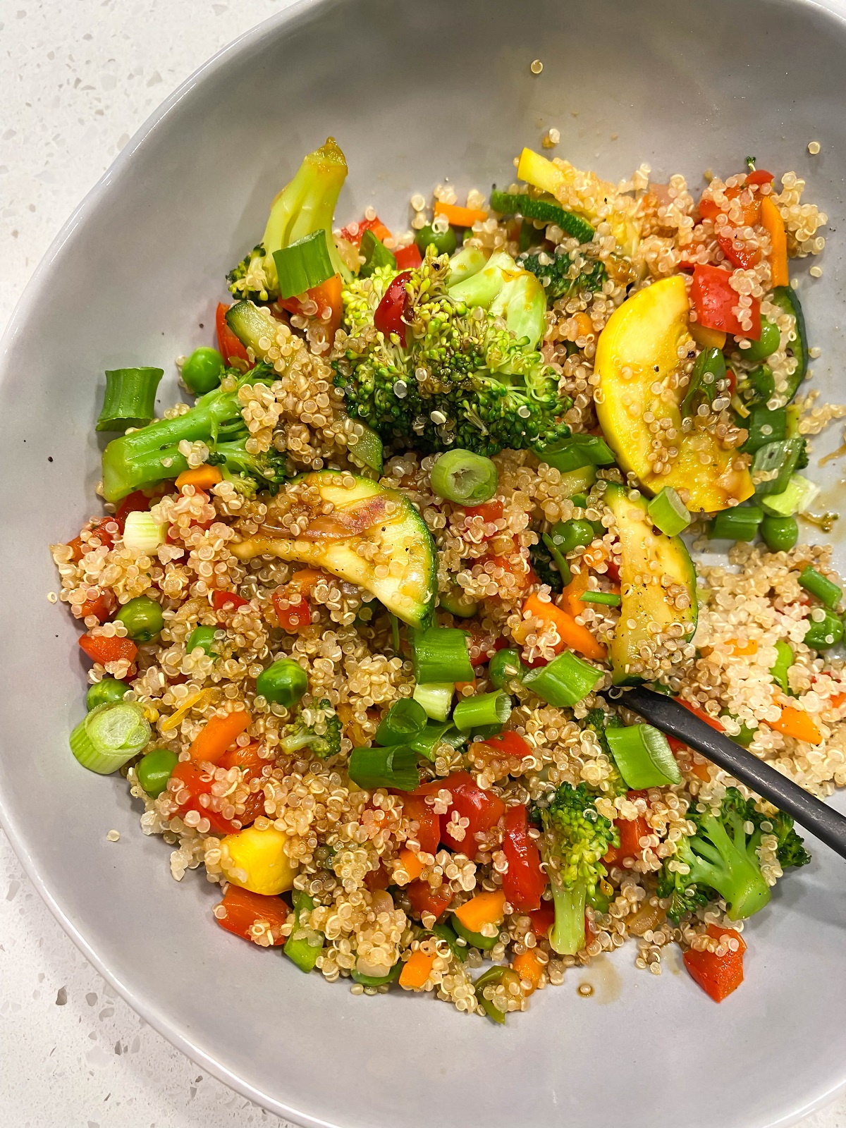 gray bowl with quinoa and colorful veggies and black fork