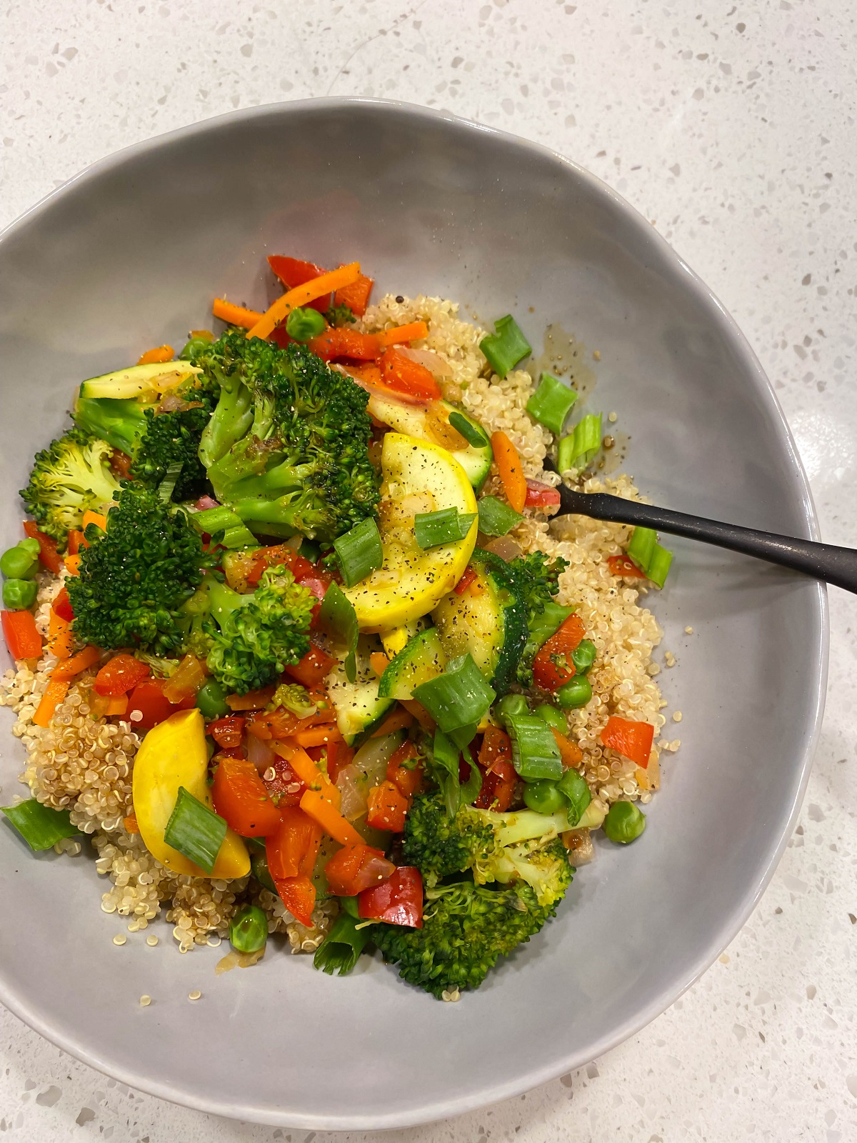 broccoli zucchini red bell pepper on top of cooked quinoa in gray bowl
