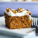 up close shot of slice of cake on white plate with frosting and walnuts on top