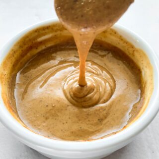 pour shot of spoon drizzling almond butter dressing in white bowl