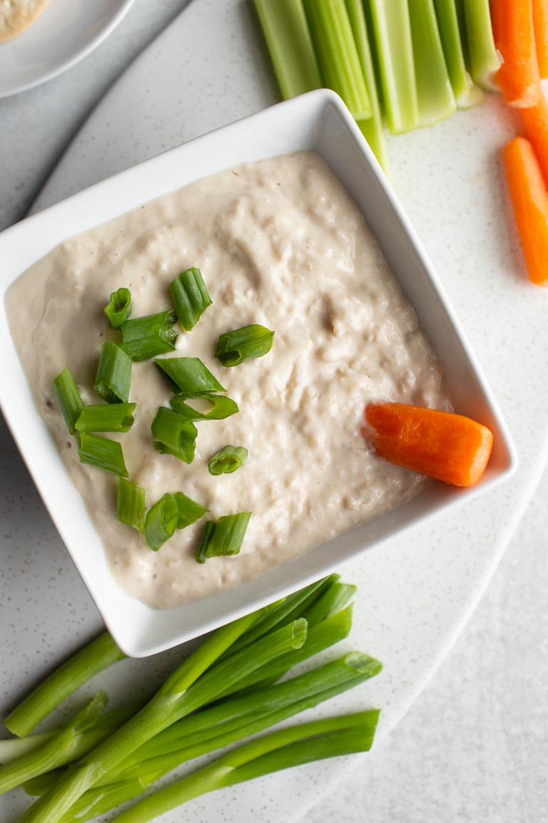closeup of dip with carrot and green onions in it in white bowl
