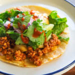 white plate with vegan taco meat and toppings on top of tortilla