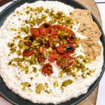 black plate with ricotta and cherry tomatoes and pistachios
