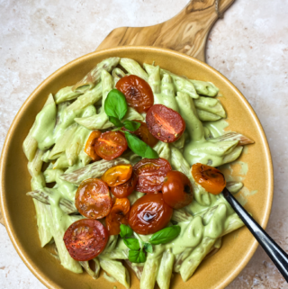 yellow bowl with basil cream sauce over pasta with cherry tomatoes