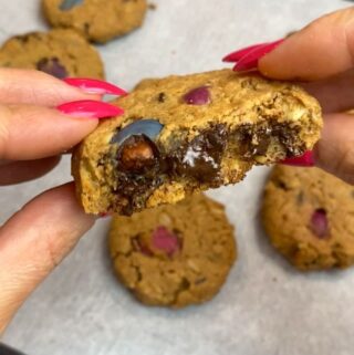hands with pink nails holding closeup vegan monster cookie